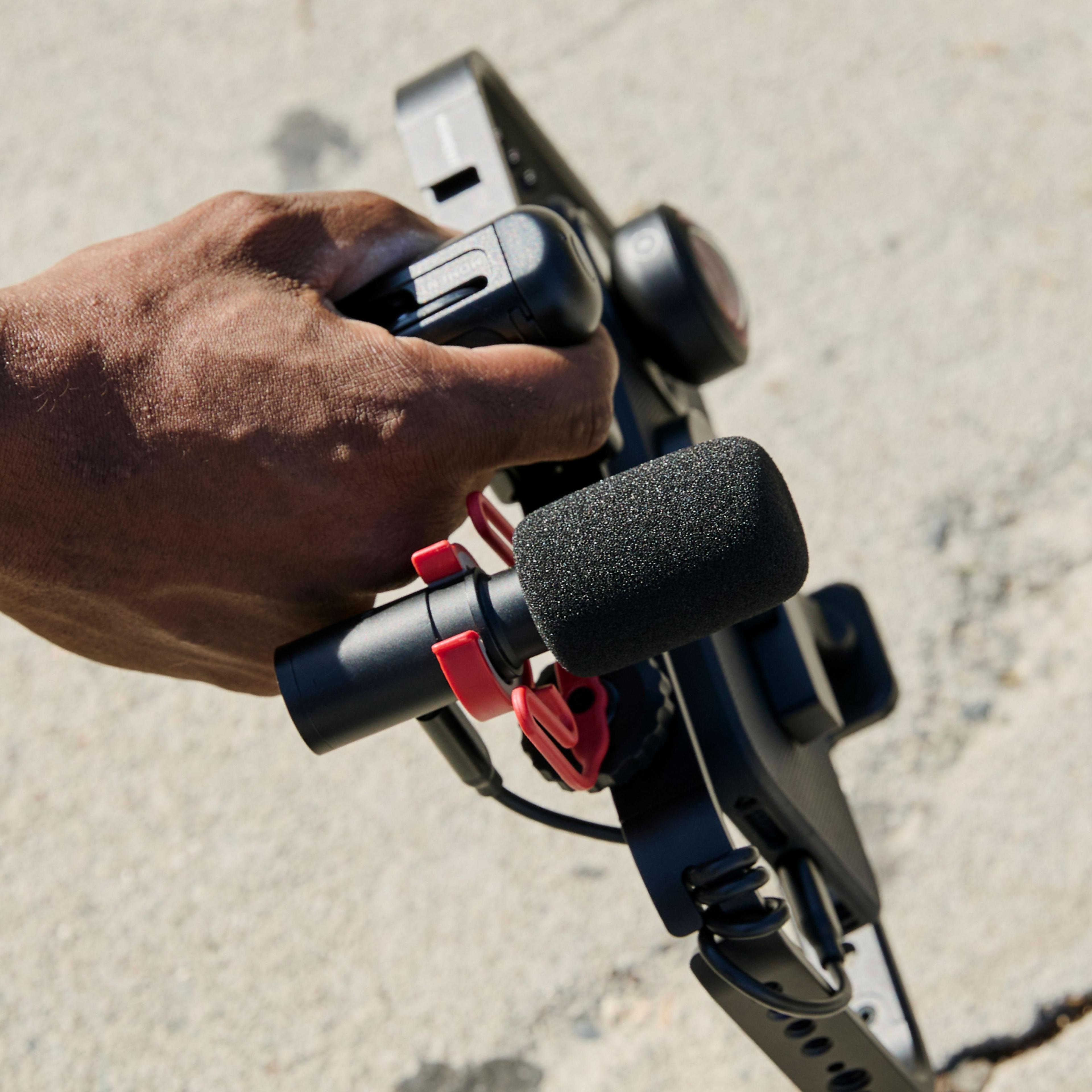 Hand holding iPhone 16 with a mobile filmmaker cage with an on-camera shotgun microphone for footage.